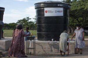 Water barrel with USAID logo, and four women washing their hands